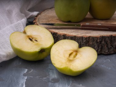 İki yeşil altın elma ve bir ahşap tabağı ve gri arka plan, pamuk beyaz peçete, bıçak üzerinde iki yarısı. Yakın çekim.