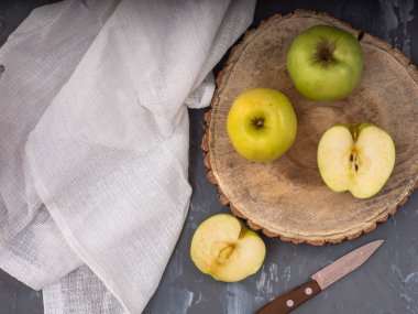 İki yeşil altın elma ve bir ahşap tabağı ve gri arka plan, pamuk beyaz peçete, bıçak üzerinde iki yarısı. Yakın çekim.