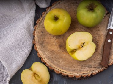 İki yeşil altın elma ve bir ahşap tabağı ve gri arka plan, pamuk beyaz peçete, bıçak üzerinde iki yarısı. Yakın çekim.