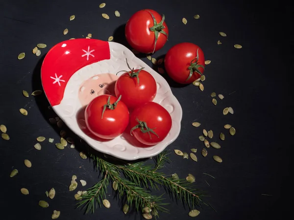 Red tomatoes with leaves on a decorative Christmas plate. Shot from above. Spruce twig for decoration.
