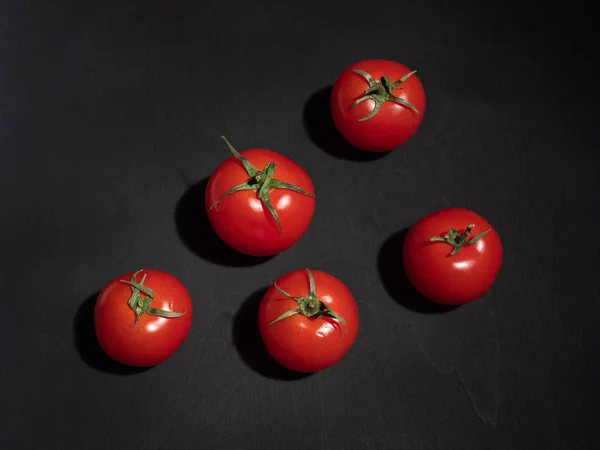 Five red tomatoes with leaves on a black background. Shot over.