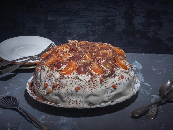 Homemade cake in a slow cooker on kefir. Decorated with fruit and whipped cream. Close-up shot from the side. In the background are saucers and cutlery.