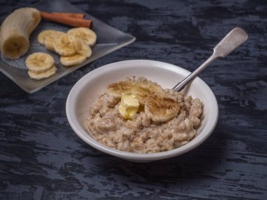 Kahvaltıda sıcak yulaf ezmesi ve dilimlenmiş muz. Arka planda bir cam dekoratif ile kıyılmış banat plakadır.