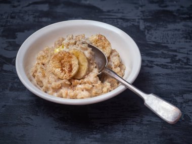Tarçın ve muz kupaları serpilir yulaf lapası derin bir tabak. Koyu ahşap arka plan üzerinde çekim yakın.