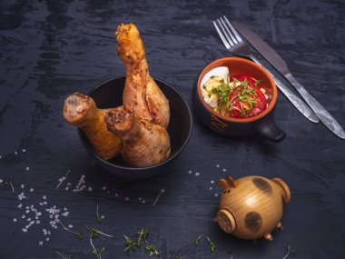 Fırında tavuk drumsticks salata domates yarım ve haşlanmış yumurta dilimleri karanlık bir arka plan üzerinde. Tuz shaker olduğunu bir ahşap domuz, serpilir kaba tuz.