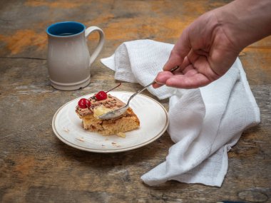 Ev yapımı kek ve çay yüksek bir kupa boş bir kaşık ile bir el bir dilim. Eski ahşap masa, pamuk beyaz peçete kompozisyonu