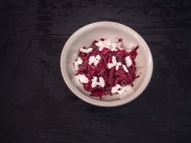 Bir derin beyaz seramik plaka siyah bir arka plan üzerinde kırmızı pancar ve beyaz peynirli salata, hafif öğle yemeği