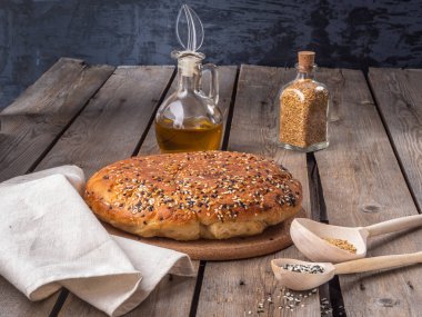 Ev yapımı ekmek ev pişmiş ile keten ve susam tohumu yalanlar üzerine bir rustik ahşap tahta masa, tahta kaşıklar tohumlar, bitkisel yağ ve cam kavanoz içinde tohum ile serpilir.