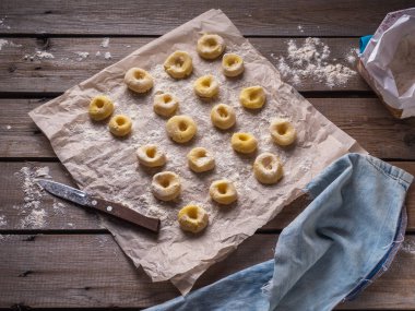 Patates gnocchi, bir denim kumaş, arka planda bir tahta masada parşömen üzerine düzenlendiği un bir çantam. Masanın üzerine dağılmış un.
