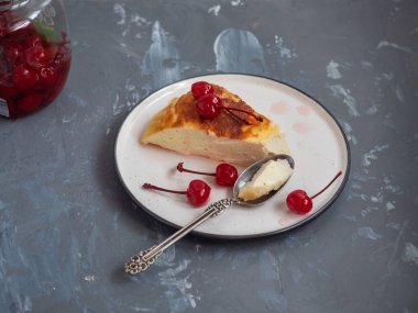 Süzme peynir güveç içinde belgili tanımlık geçmiş bir kavanoz kiraz gri bir arka plan üzerinde bir şekilde dekore edilmiş konserve kiraz ile seramik bir daire üzerinde bir parça