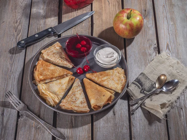 Pancake gri bir plaka üzerinde bir üçgen ile haddelenmiş, ekşi krem ve konserve kiraz, büyük bir elma, kiraz ve sofra ve keten peçete bir kavanoz ile küçük krep bir dizi e yayıldı