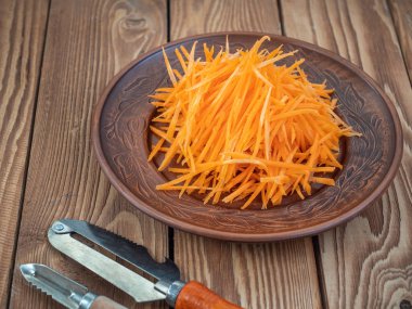 Bir seramik plaka üzerinde ham havuç Julienne Julienne yakın yukarı, bir soyucu yanında