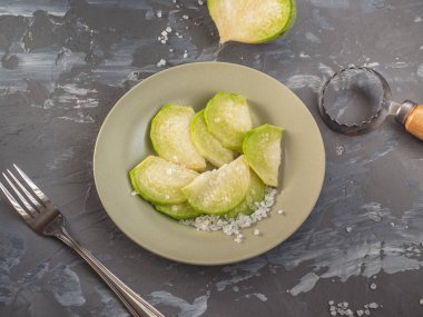 dilimlerin içine dilimlenmiş taze yeşil turp bir seramik zeytin plakası üzerinde yatıyor, bir çatal ve bir soyucu gri lekeli arka plan yanında
