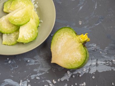 dilimlerle dilimlenmiş yeşil turp ve kaba tuz ile serpilir yarı yarıya kesilmiş turp sağ alt köşesinde bir seramik plaka üzerinde yatıyor, dar bir mesafeden kaldırıldı