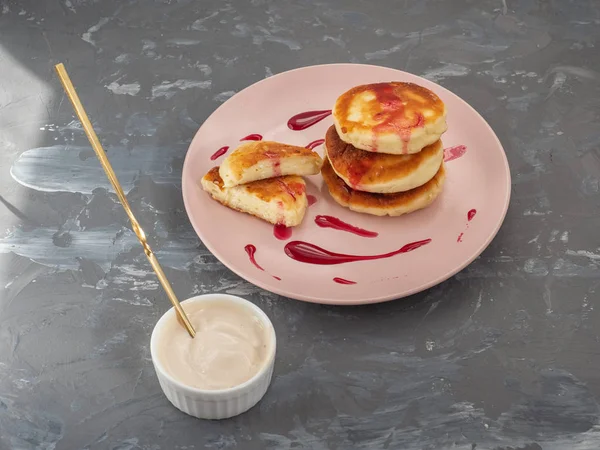 Tartas de queso caseras en un plato de cerámica rosa, en primer plano un tazón de helado blanco con un trineo y cuchara de postre — Foto de Stock