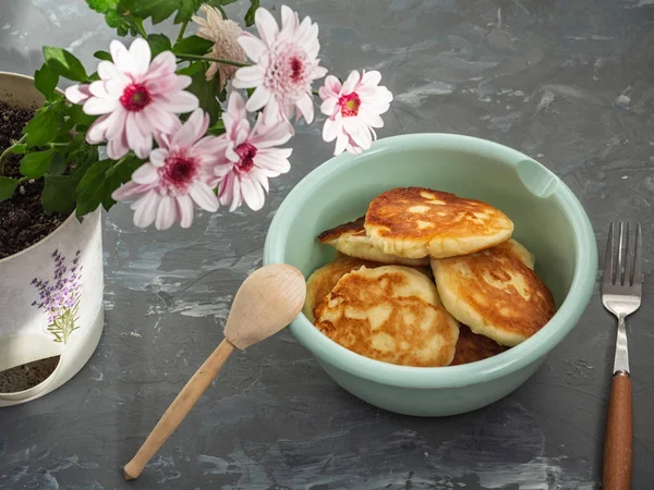 Pasteles de queso hechos en casa en un plato profundo con cubiertos de madera sobre un fondo gris, crisantemo en el fondo — Foto de Stock