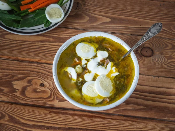 Весенний суп со свежими травами, одетый со сметаной в глубокую тарелку на деревянном фоне — стоковое фото