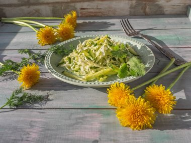 Yuvarlak bir salata tabağı üzerinde baharatlı otlar ile taze katusta ve salatalık ile Vegan salata, kurulu masada birkaç çiçekli karahindiba