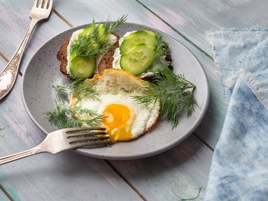 Lor peyniri ve taze salatalık sandviç sandviç, taze otlar, hafif bir kahvaltı ve sofra ve bir tahta tepsiüzerinde denim peçete için gri bir seramik plaka üzerinde omlet. Çekim yakın, üst görünüm.