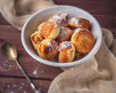 Pudra şekeri serpilir derin beyaz bir tabakta ev yapımı cheesecakes. Bir bej peçete ve bir çay kaşığı kompozisyon tamamlayın. Yakın mesafeden çekilmiş.