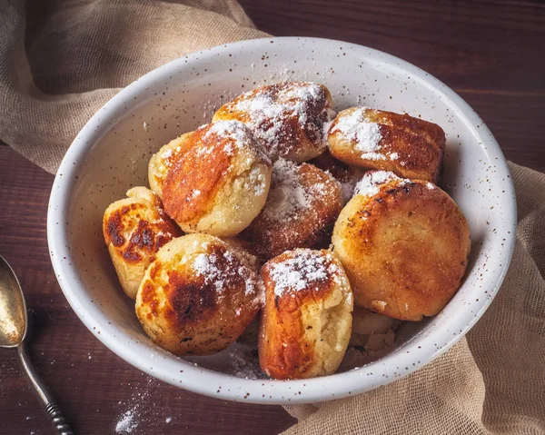 Ahşap bir tepsi üzerinde derin beyaz bir tabakta ev yapımı cheesecakes. Bir bej peçete ve bir çay kaşığı kompozisyon tamamlayın. Yakın mesafeden çekilmiş.
