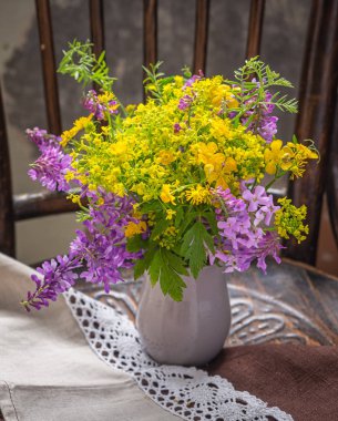 Rustik bir iç eski bir sandalyede bir toprak gri vazo sarı ve mor yabani çiçekler Yaz buketi