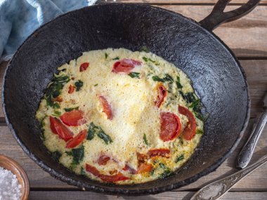 Eski bir Tahta masada yuvarlak dökme demir tavada domates ile Omlet, bir kil tuz shaker pamuk peçete ve kaba tuz, masa bıçağı, yakın mesafeden alınan