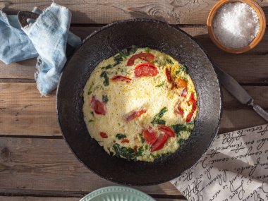 Eski bir tahta masada yuvarlak dökme demir tavada domates ile Omlet, bir kil tuzluk pamuk peçete ve kaba tuz