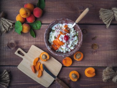 Koyu ahşap masa, mutfak Kurulu ve bıçak üzerinde derin bir seramik tabakta taze kayısı ve kiraz ile rustik süzme peynir kahvaltı, üst açıdan vuruldu