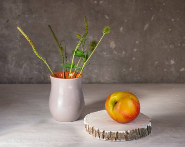 Beyaz arka plan üzerinde olgun nektarinler, küçük gri seramik vazo da ahşap bir disk ve çayır otları