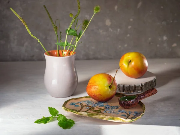 Rijpe nectarines op een witte achtergrond met keramische gerechten en weide kruiden in een keramische grijze vaas — Stockfoto
