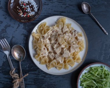 Kahvaltı makarna ve gri bir arka plan üzerinde taze salatalık salatası, çatal ve kaşık, küçük bir tabak üzerinde baharatlar,