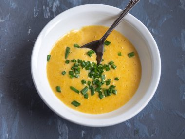 Sebze ve peynir ile patates püresi çorbası derin beyaz tabak yeşil soğan ile serpilir, gri bir arka planda bir çorba kaşığı, yakın mesafeden vurdu