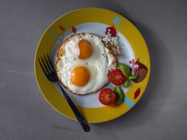 İki yumurtalı hızlı kahvaltı. omlet. gri arka planda yuvarlak plaka üzerinde domates.