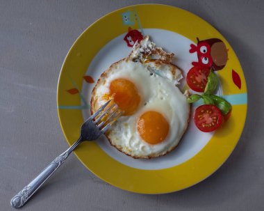 İki yumurtadan hızlı bir kahvaltı, gri bir arka planda yuvarlak bir plaka üzerinde domates ile omlet, üst açıyla vurdu