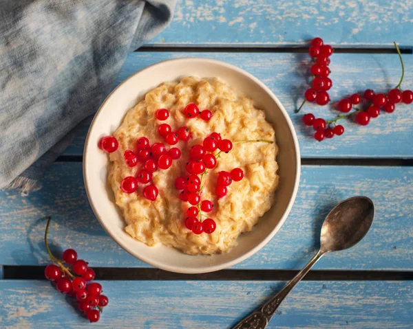 Oatmeal for breakfast with red currants on a blue wooden tray, spoon and denim napkin