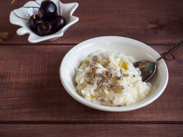 White breakfast of rice milk porridge with sunflower seeds and cherry berries in white wafers and a spoon on a wooden tray