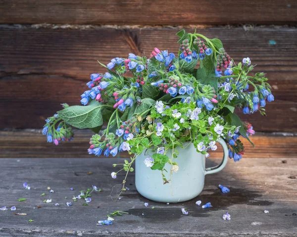 Ramo de flores de campo azul pradera pequeña en una taza esmaltada en el porche de una casa de pueblo — Foto de Stock