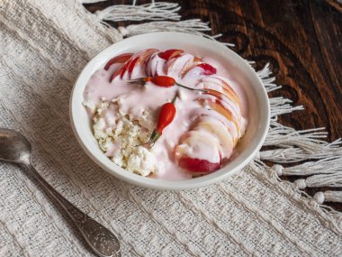 Nektarinler ve gül kalçalı beyaz örme masa örtüsü üzerinde beyaz derin bir tabakta ekşi krema ile köy peyniri,