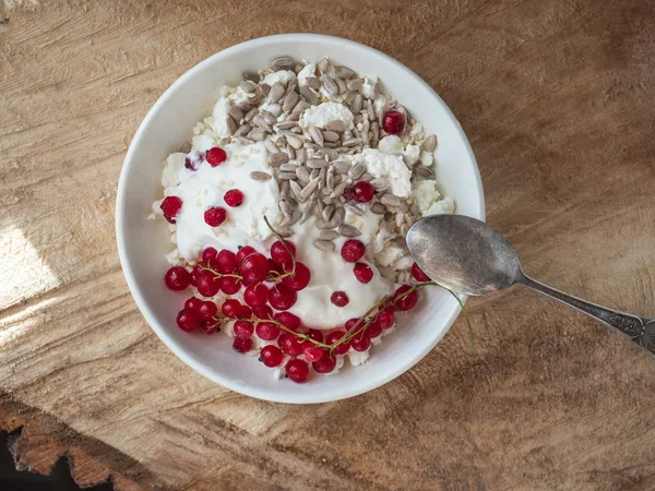 Ein leichtes und schmackhaftes Frühstück mit hausgemachtem Quark, Samen und Beerenmarmelade in einem weißen Teller auf rauem Holzgrund aus der Nähe — Stockfoto