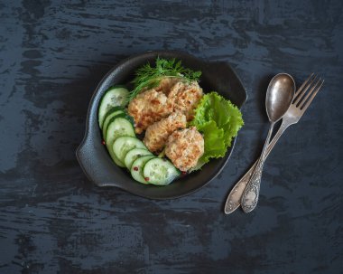 Pirzola, marul ve taze salatalık ve çatal bıçak takımı nın koyu zeminüzerine siyah bir tabak ta kahvaltısı, üst tegörüş