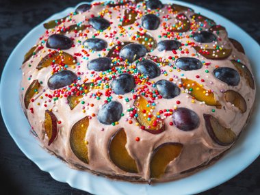 Siyah bir masada beyaz bir tabak üzerinde meyve ve ekşi krema ile ev yapımı kek, üst görünümü