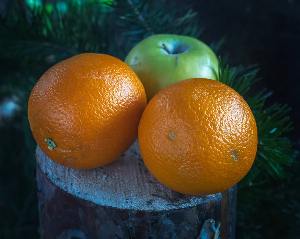 Fruit set of oranges and green Apple lies on a stump under a pine tree