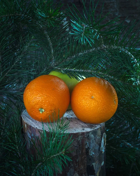 Fruit set of two oranges and a green Apple lies on a stump under the branches of pine