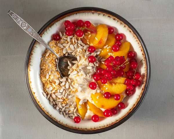 Healthy fitness Breakfast of oatmeal with berries, fruits and cereals in a deep plate and spoon on a gray background,