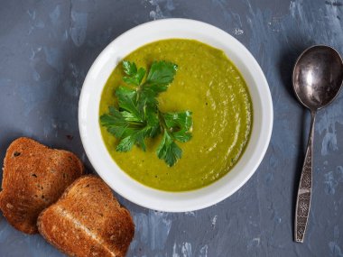 Gri bir arka plan üzerinde derin beyaz bir tabakta bezelye çorbası püresi