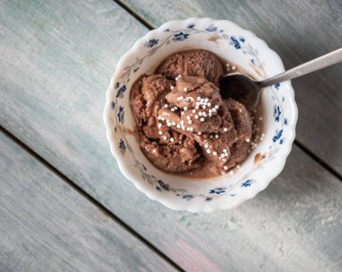 Çiçek desenli küçük bir kâsede ev yapımı çikolatalı dondurma ve gri arka planda çay kaşığı, üst manzara, bulanık odaklanma.