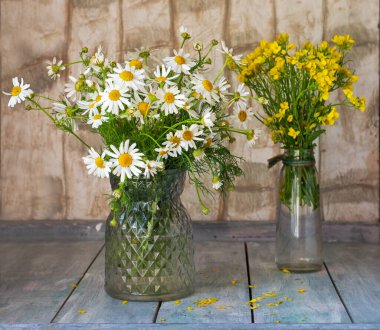 İki vazoda kır çiçekleri var. Papatyalar ve yaz çiçekleri kırsal bir masa üzerinde süperler.