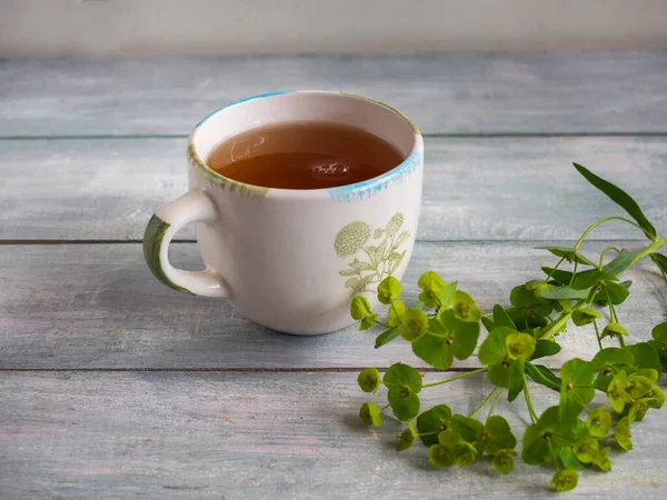 Cup of tea in a light mug with a delicate pattern with a green sprig on a blue wooden table