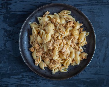 Kabuk şeklinde makarna ve siyah bir arka planda siyah bir tabakta tavuk eti.